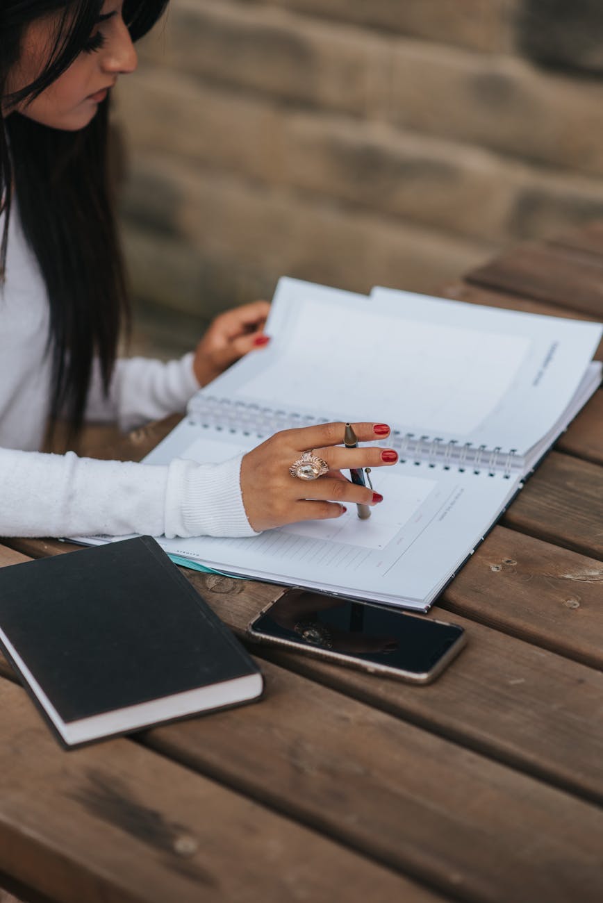 crop ethnic office worker with copybook at wooden table